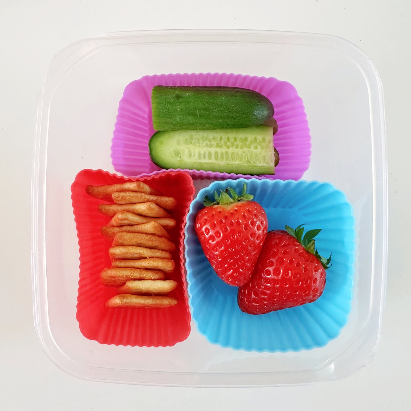 silicone cupcake mould in red, blue and purple containing strawberries, sliced mini cucumber and mini cheese crackers.