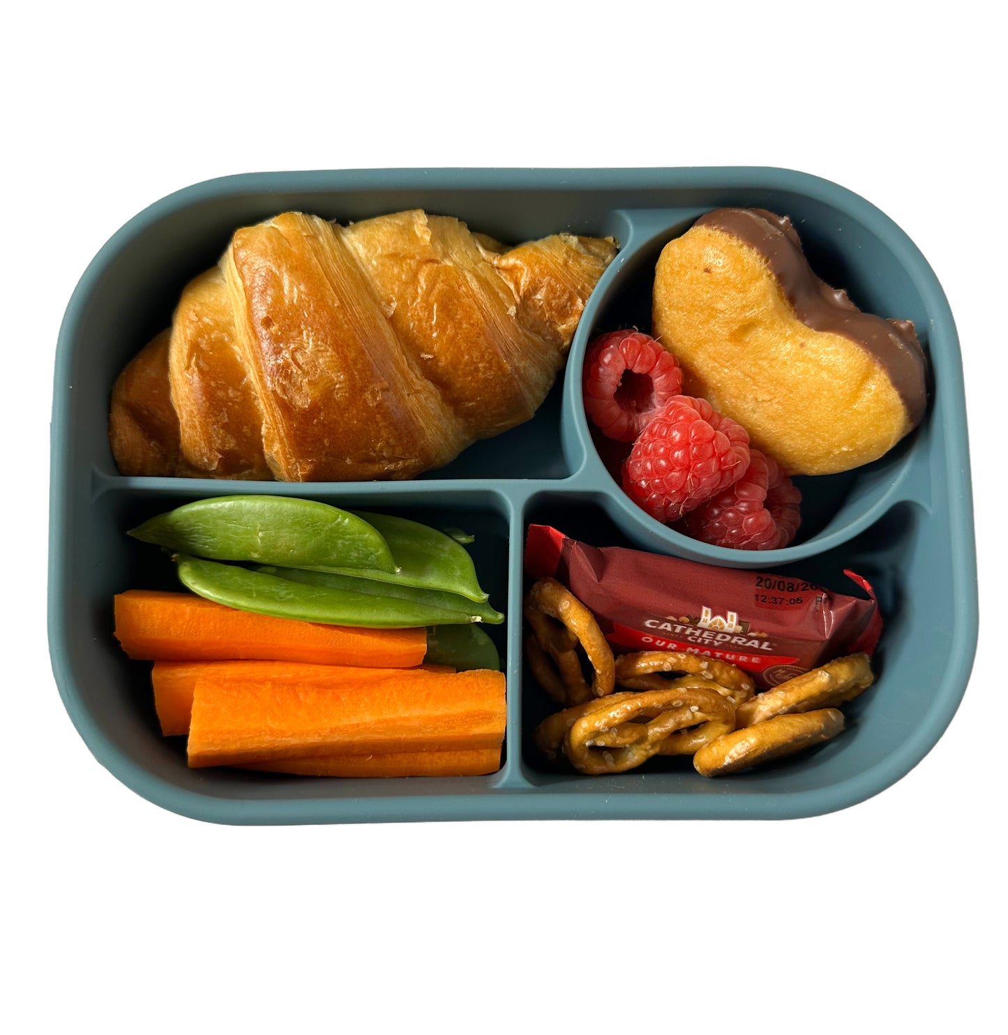 a blue kids silicone lunchbox with sections filled with a croissant, sugar snap peas, pretzels, a mini Cathedral City cheese, a heart shaped cake and raspberries.