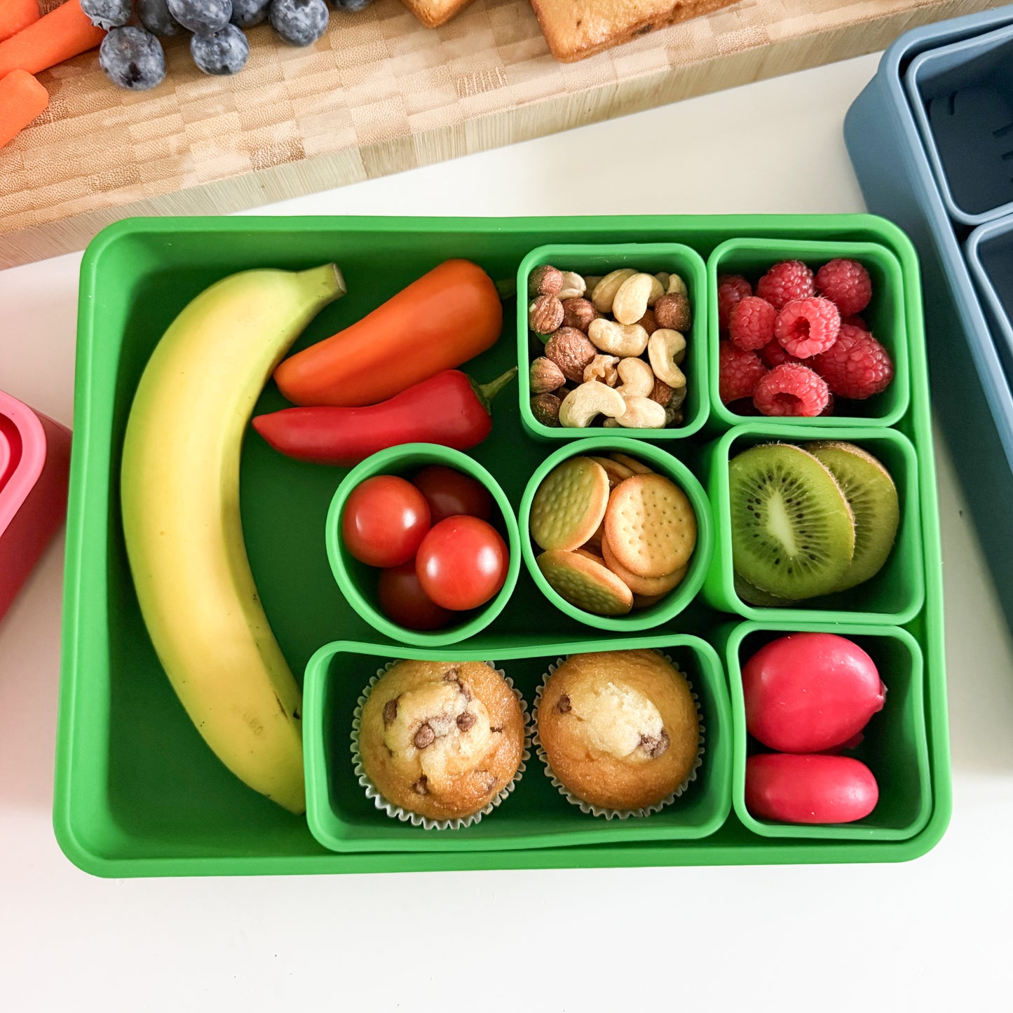 A large green silicone box with 10 separate and removable compartments that have been filled with snacks.