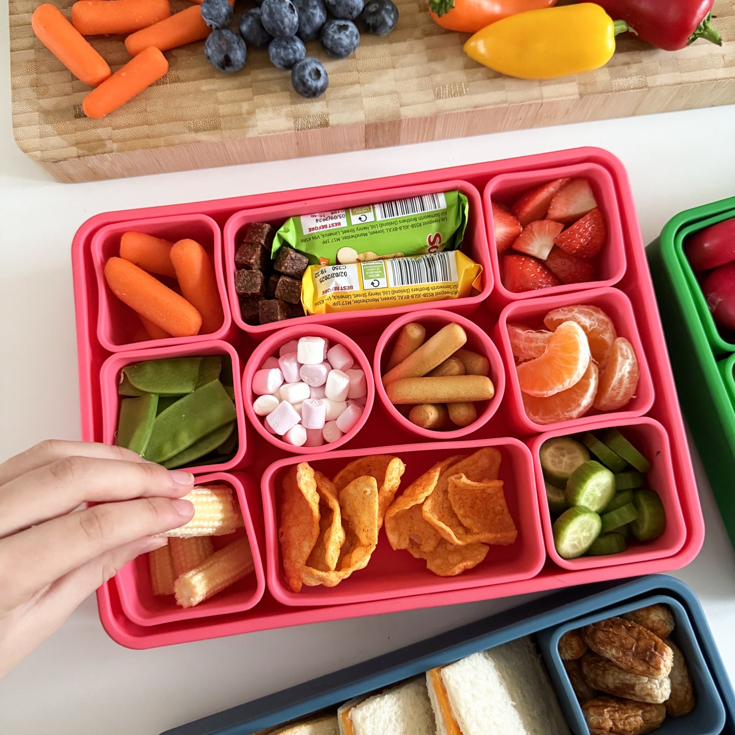 A large pink silicone box with 10 separate and removable compartments that have been filled with snacks.