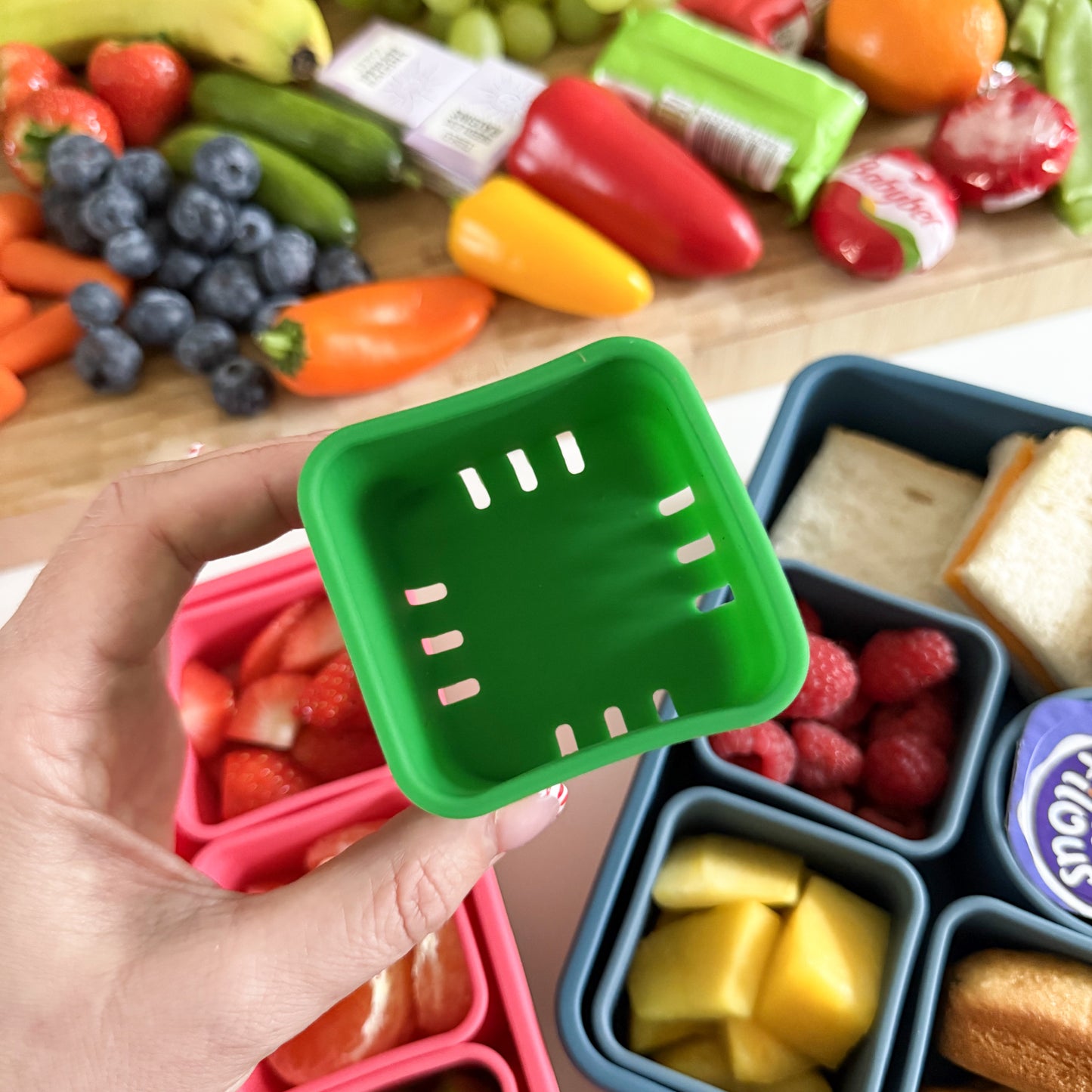 green snack box compartment with slits in the bottom, so you can rinse fruit and veggies and place them in, allowing any excess water to drain to the bottom of the box.