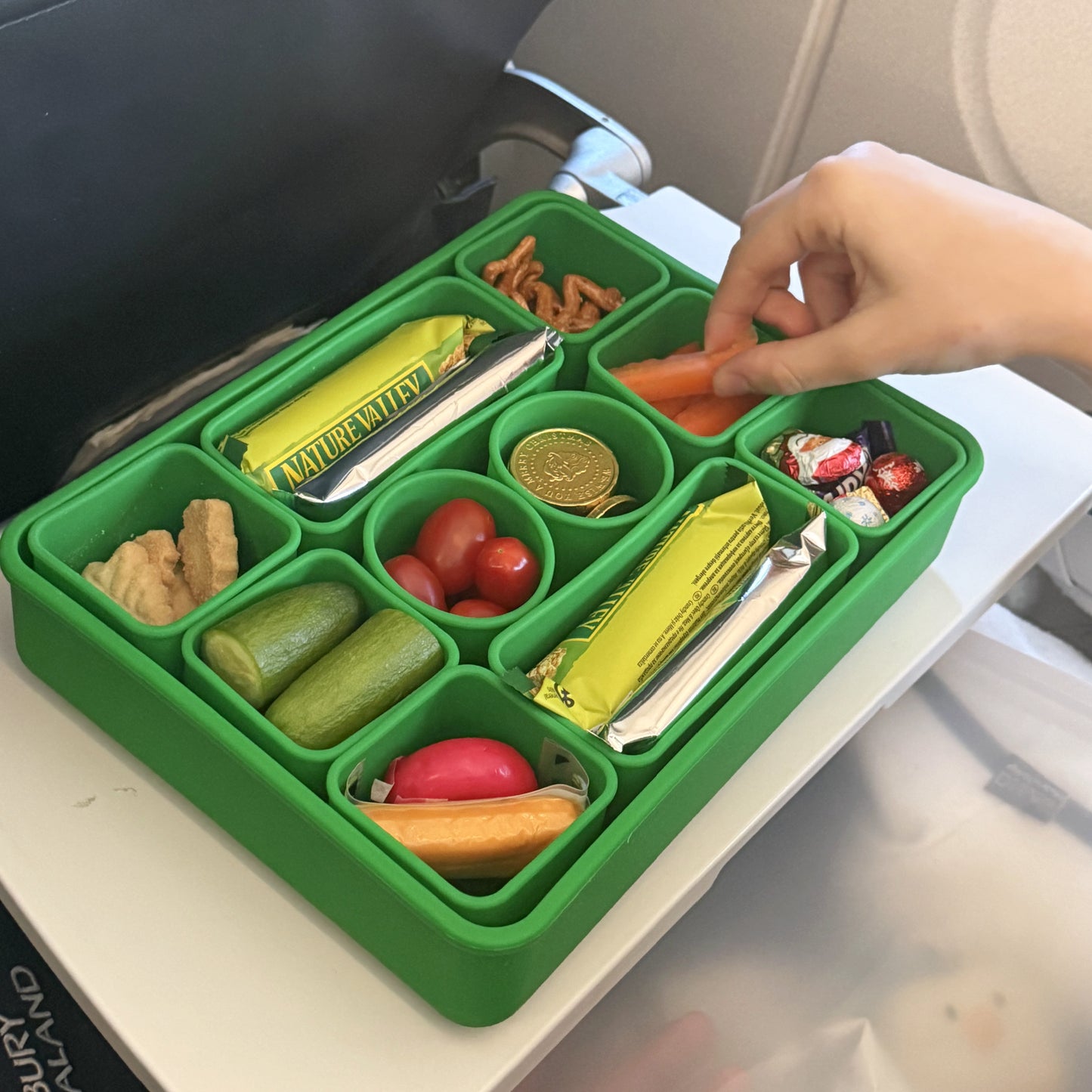 Large 10 Compartment snack box filled with snacks on an aeroplane seat tray.