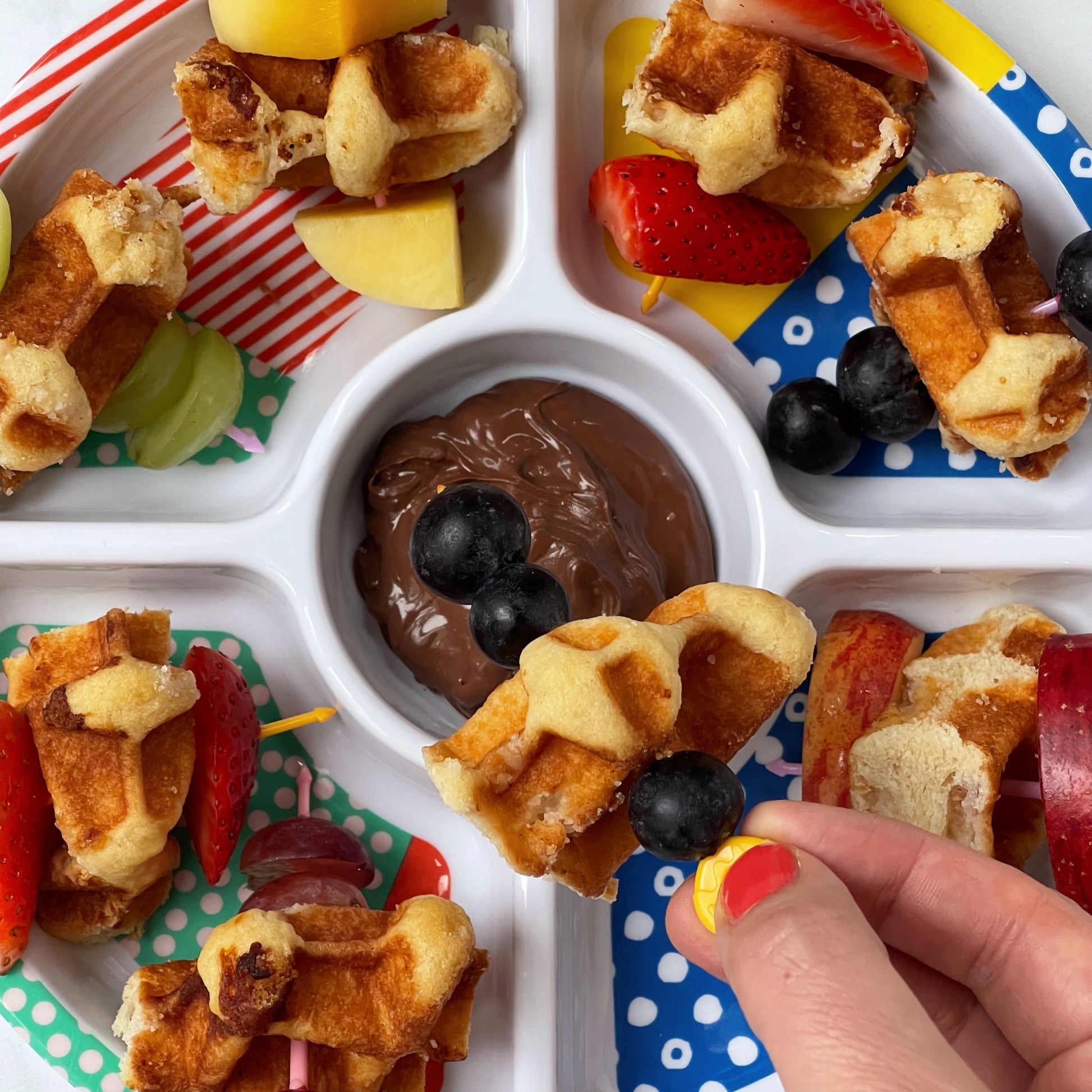 Pick Stick Pastels bring used for waffles and fresh fruit in a children's divided plate with chocolate sauce.