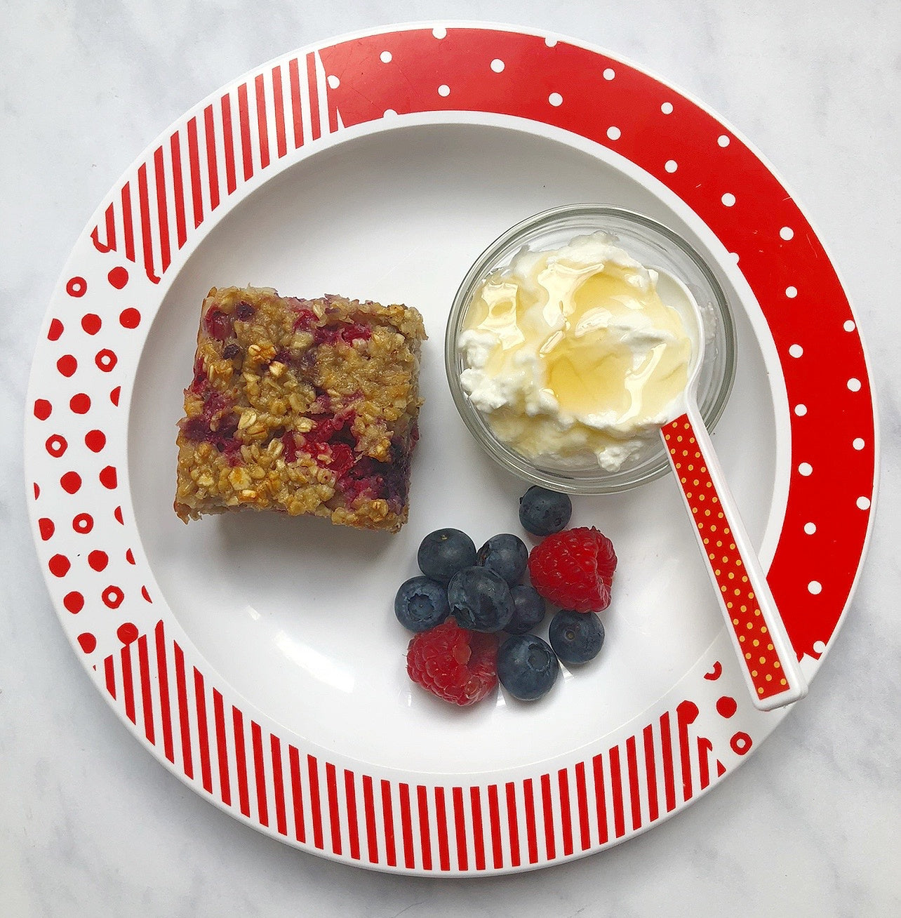 Kids classic plate with a breakfast bar, fresh berries and a serving of yogurtand honey on it.