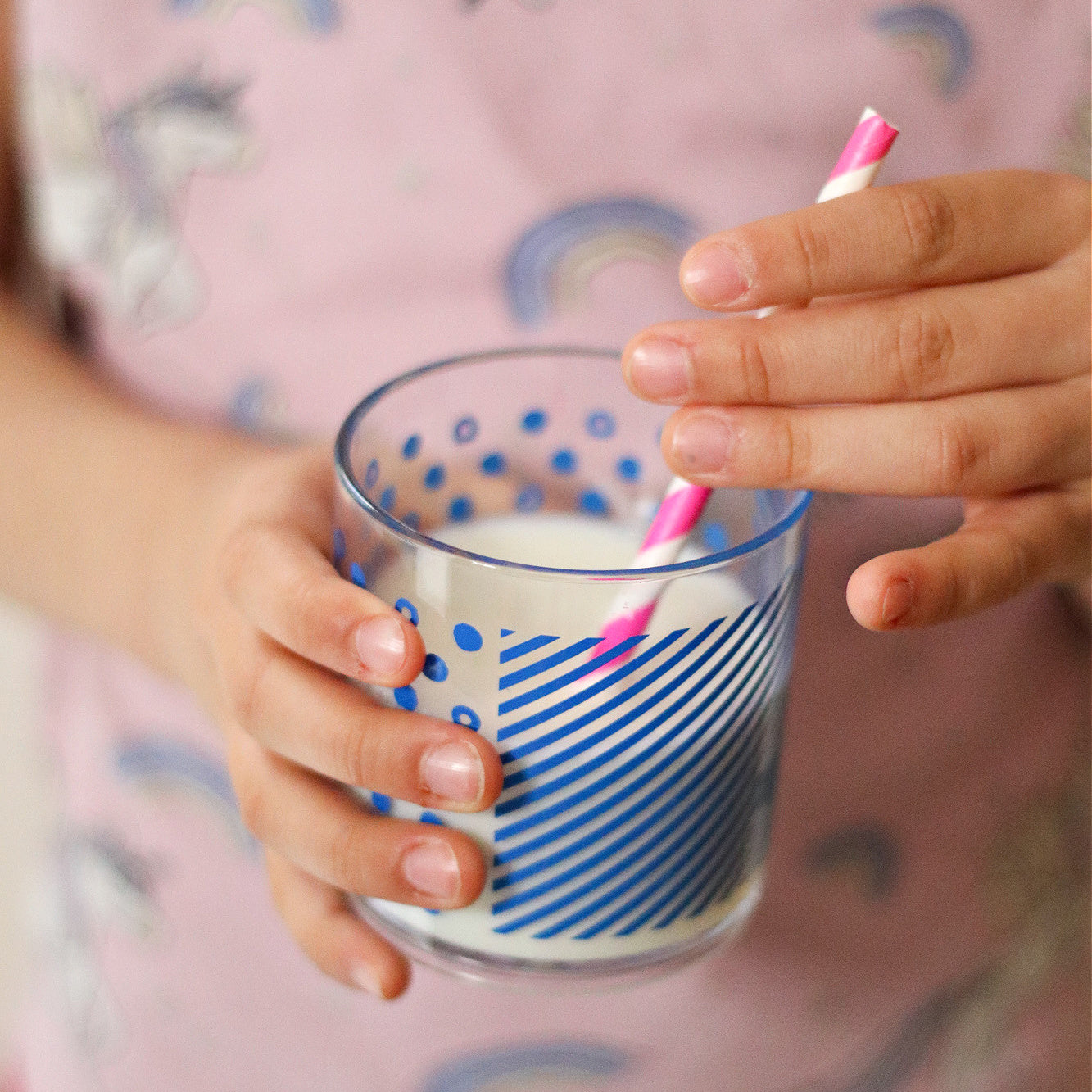 a childs hand holding the classic tumber filled with milk and the pink and white striped straw.
