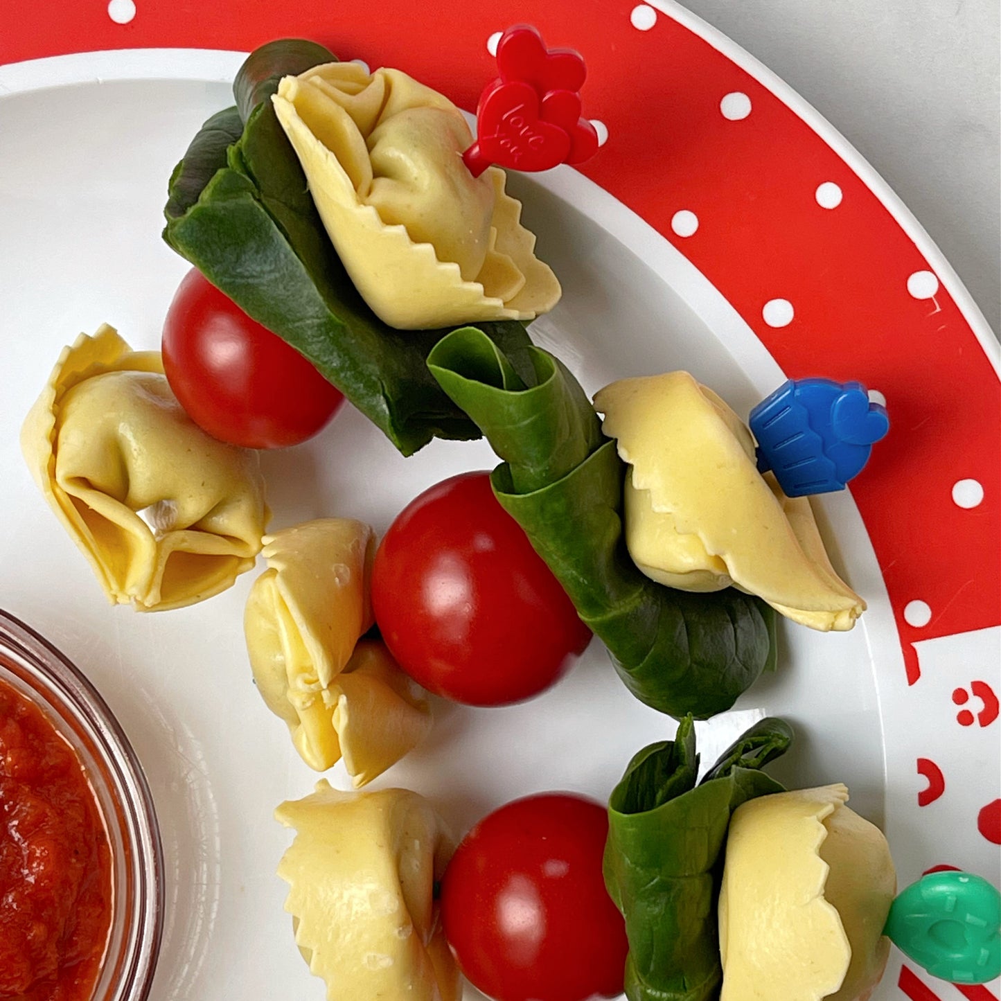 A Red, blue and Green Pick stick with tortelloni, cherry tomato and basil leaves on each of the skewers.
