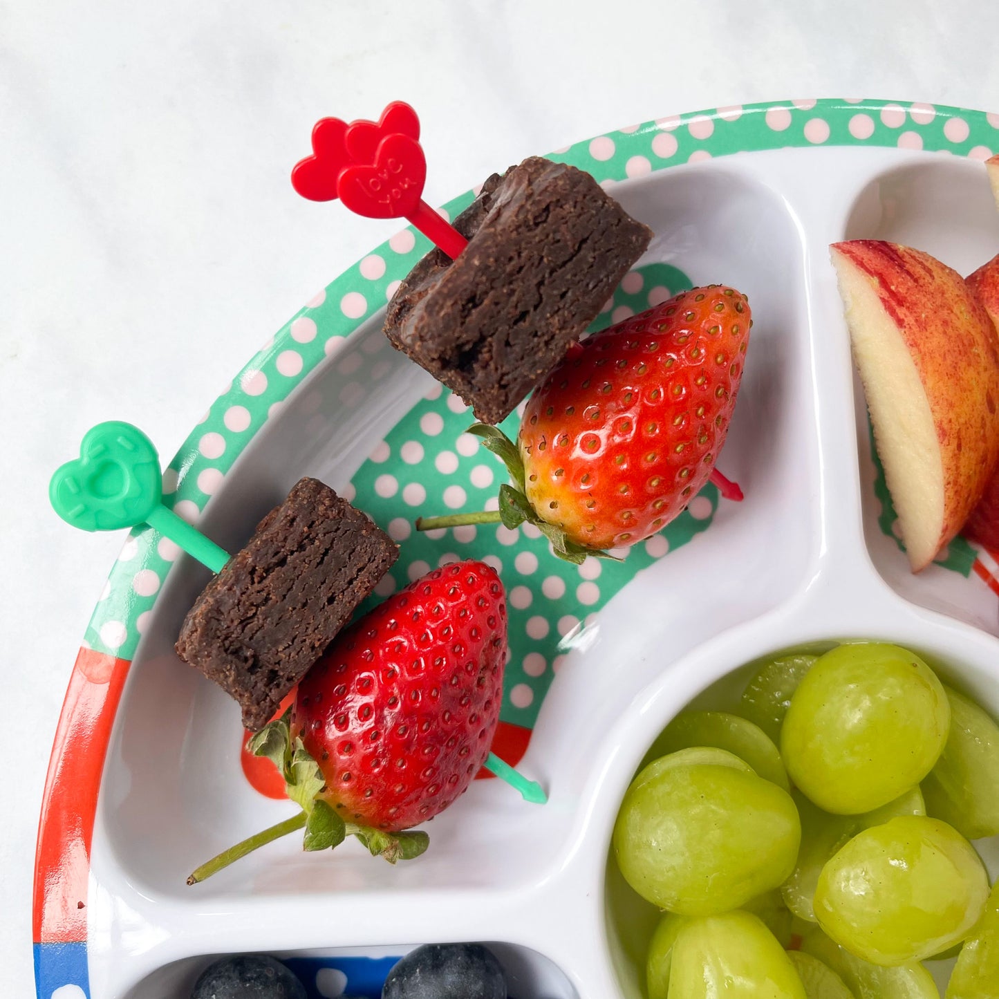 A red and green Pick Stick with a brownie square and strawberry on each skewer.